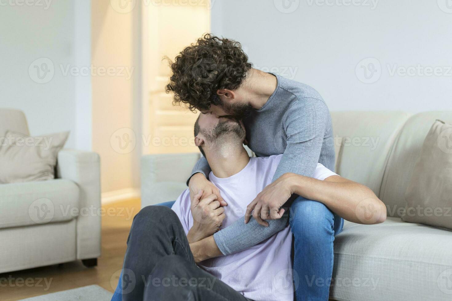 lief homo paar zoenen terwijl zittend in hun leven kamer Bij huis. twee romantisch jong mannetje geliefden hebben pret binnenshuis. jong homo paar leven samen. foto