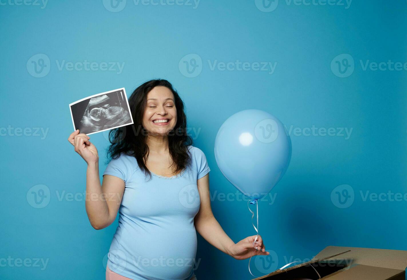 opgewonden zwanger vrouw uitdrukken positief emoties ervan uitgaand baby jongen, Holding baby echografie en blauw ballon foto