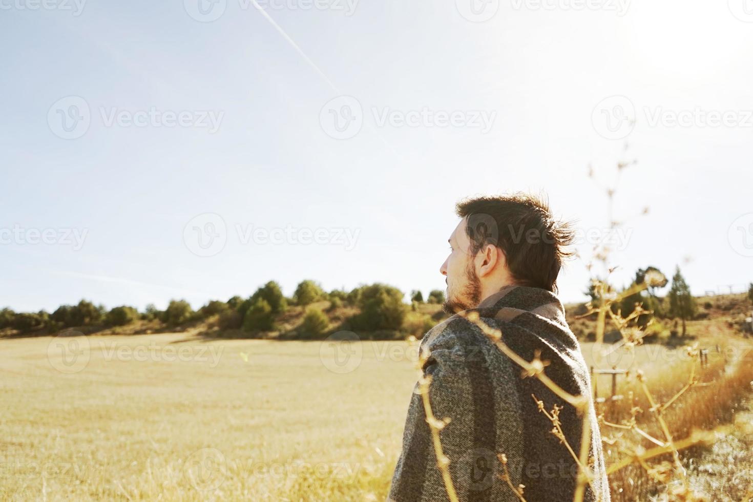 een jonge man staand van achteren genietend in de rust van de ochtendherfstzon in een pad van een geel veld met de achtergrondverlichting van de blauwe lucht foto