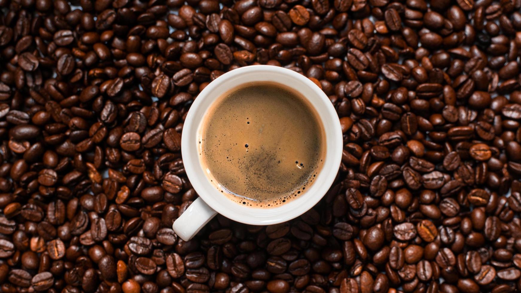 bovenaanzicht van kopje koffie in stapel koffiebonen foto