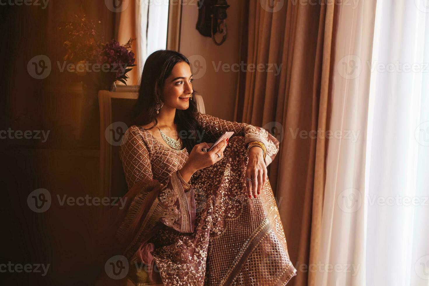rijk mooi Indisch vrouw in luxe etnisch kleren gebruik makend van haar telefoon in een 5 ster hotel kamer. gefilterd portret in gedempt kleuren, film fotografie stijl foto