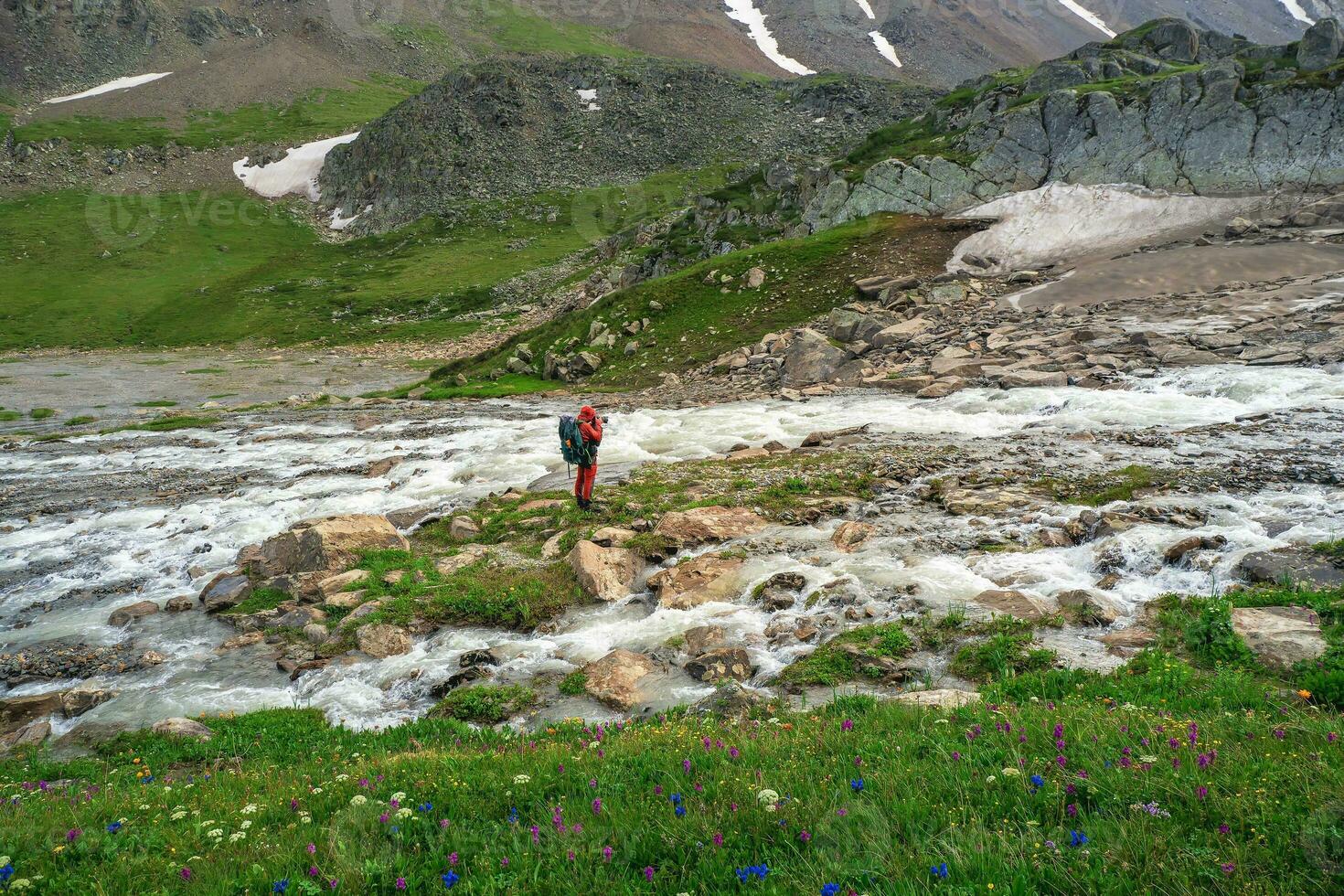 professioneel fotograaf schiet een landschap staand Aan een klein groen eiland in de midden- van een stormachtig berg rivier. groen alpine hooglanden foto