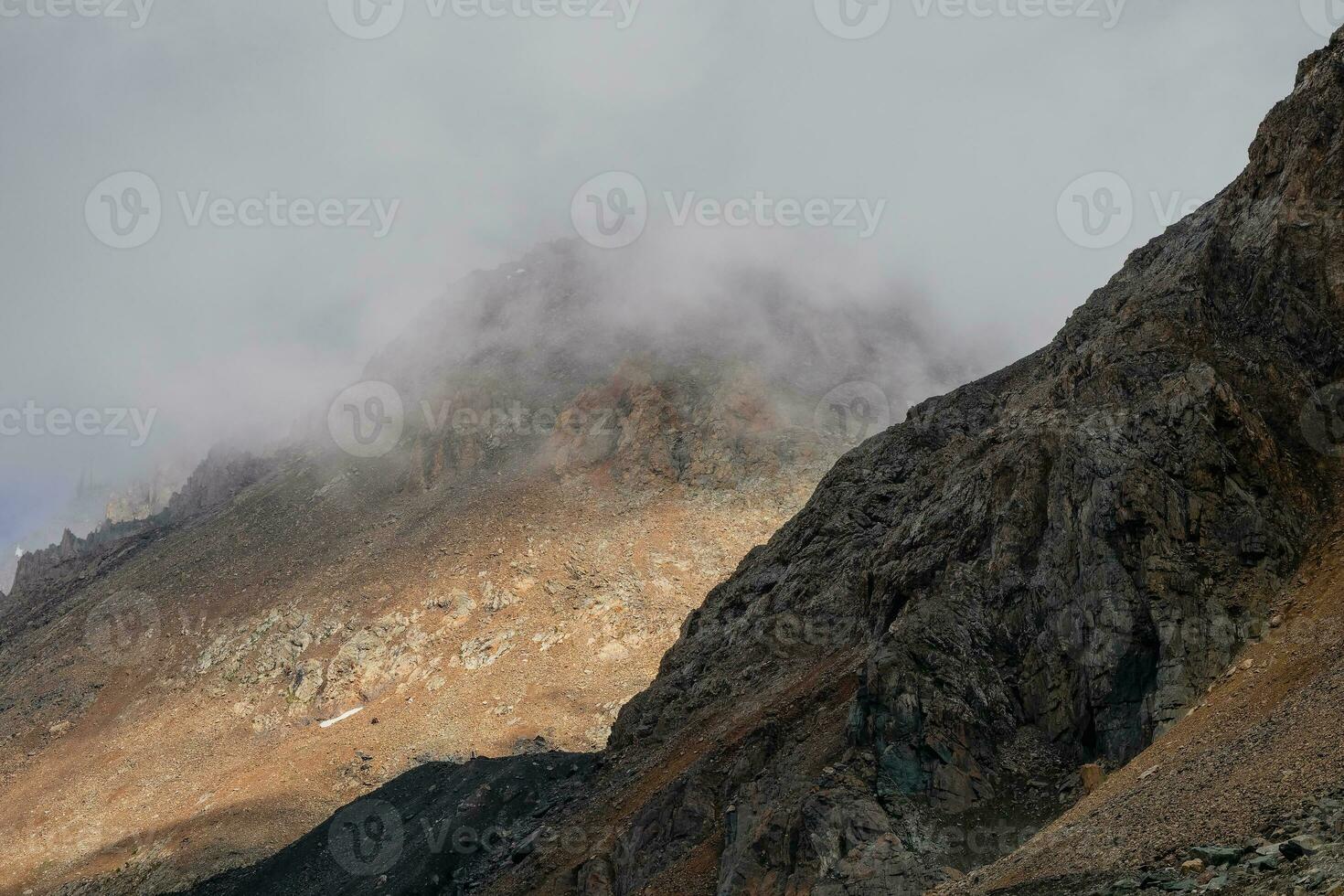 sfeervol spookachtig landschap met wazig silhouetten van scherp rotsen in laag wolken. dramatisch visie naar groot bergen wazig in regen nevel in grijs laag wolken. diagonaal helling van de berg. foto