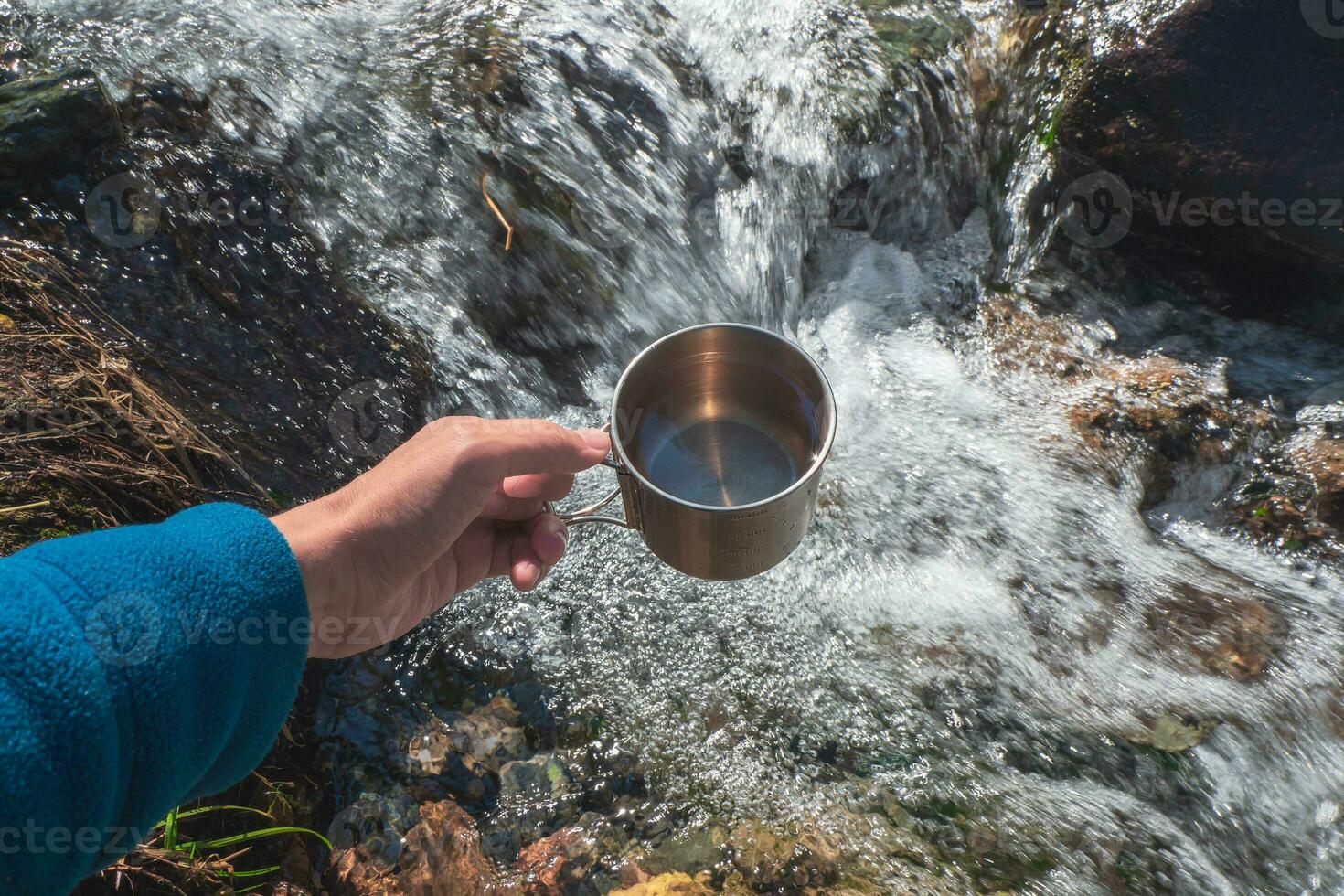 mok met zuiver glaciaal water van een berg stroom. hand- Holding een wandelaars kop met schoon drinken water. foto