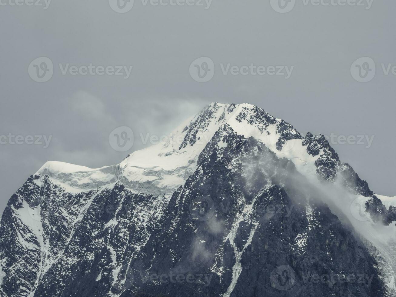 sfeervol alpine landschap met met sneeuw bedekt berg top onder sneeuw grijs lucht. geweldig landschap met mooi puntig top met sneeuw en hoog besneeuwd berg muur met laag wolken. foto