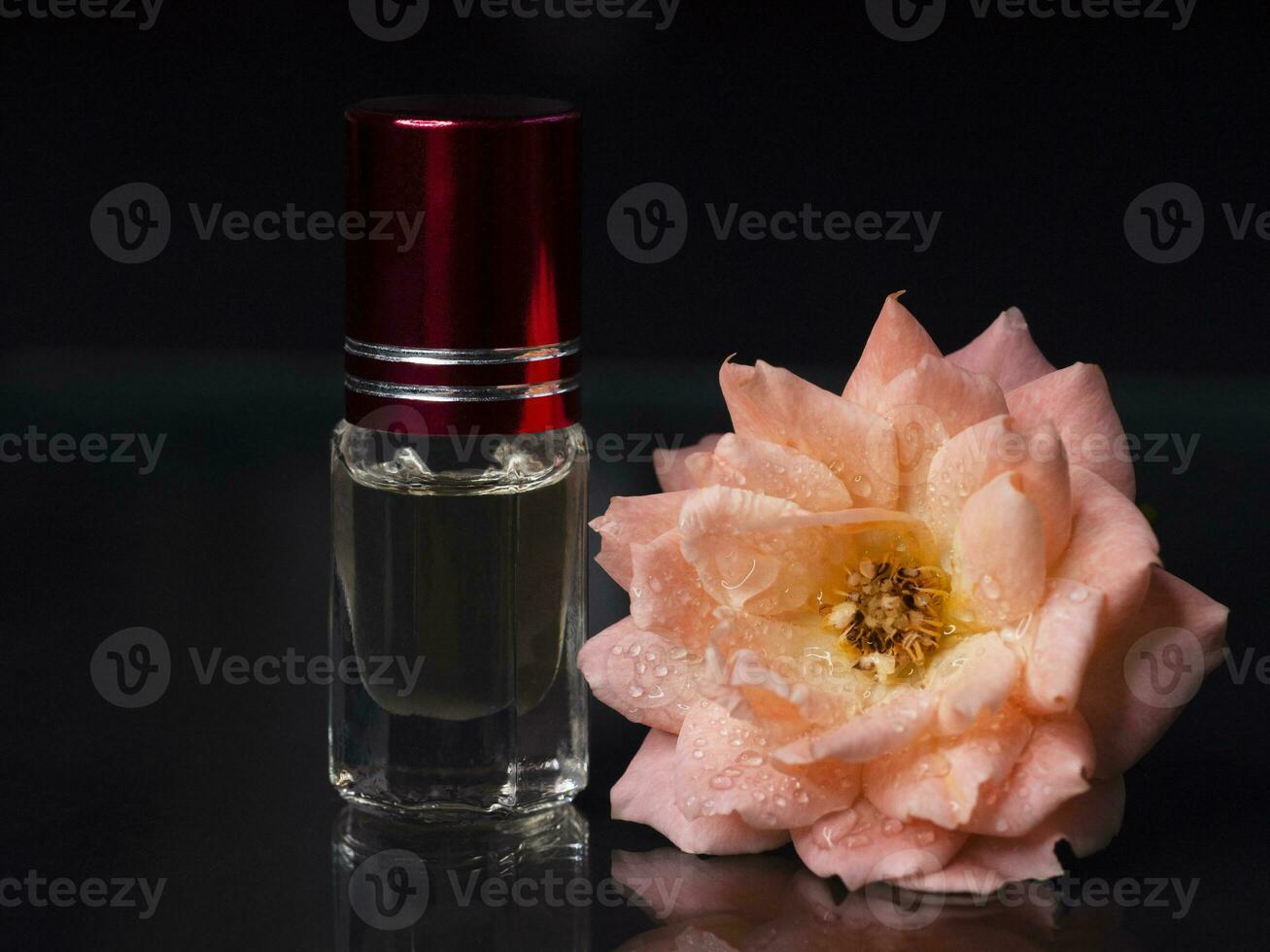 geconcentreerd parfum in een mini fles met roze geparfumeerd thee roos Aan de zwart achtergrond foto