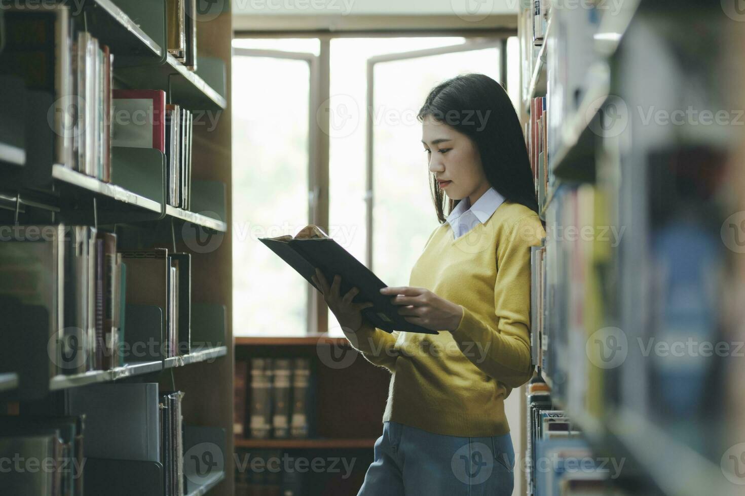 leerling staand en lezing boek Bij bibliotheek. foto