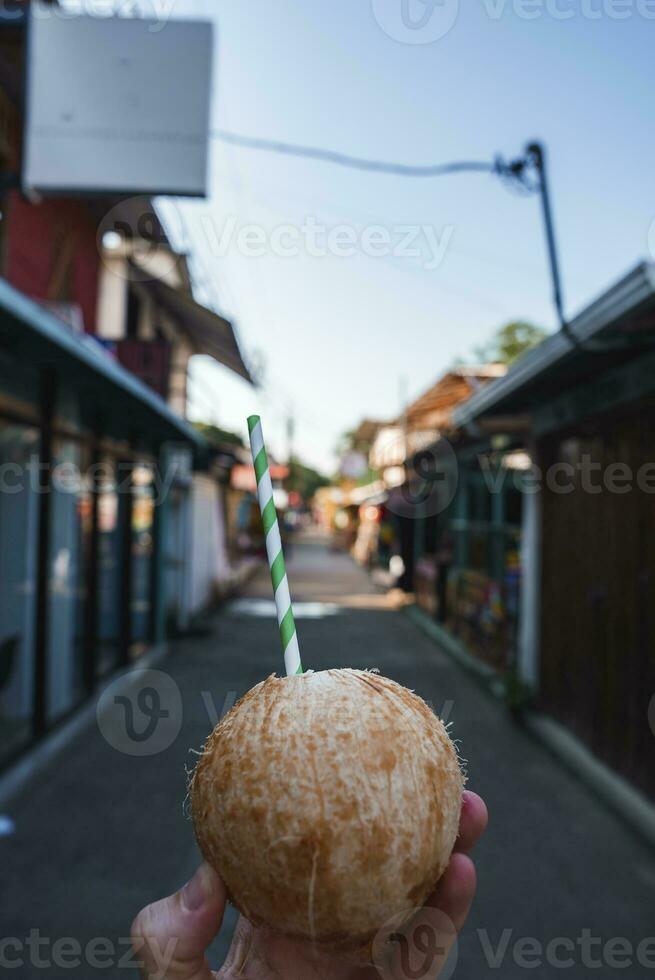 menselijk hand- Holding verfrissend kokosnoot met drinken rietje in oud stad- foto