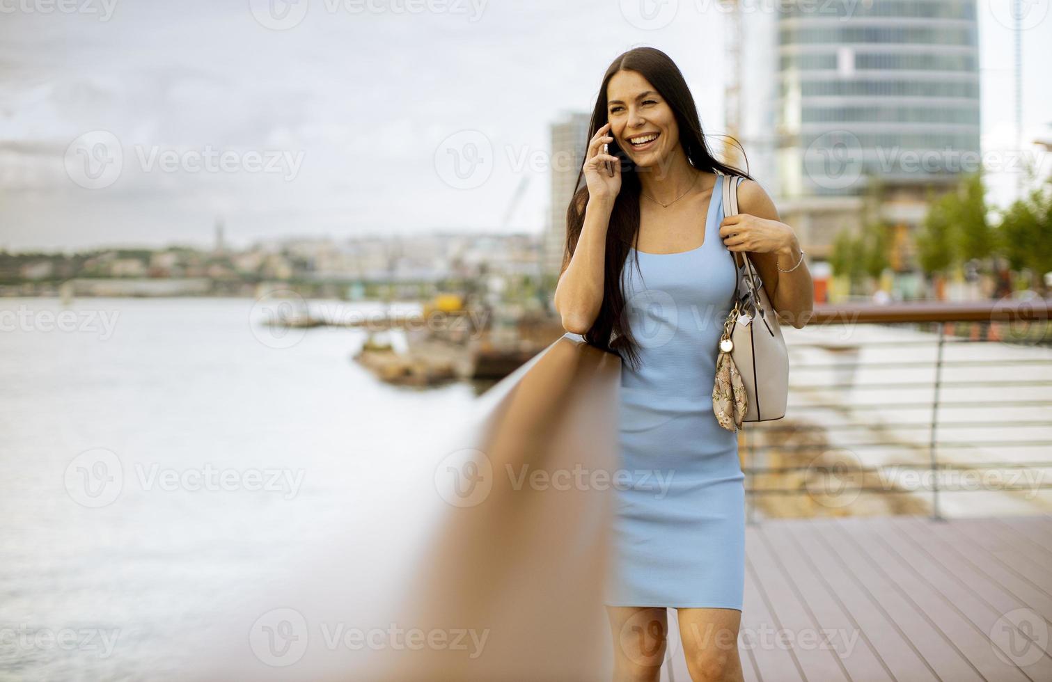 jonge vrouw met behulp van een mobiele telefoon terwijl ze aan de rivierpromenade staat foto