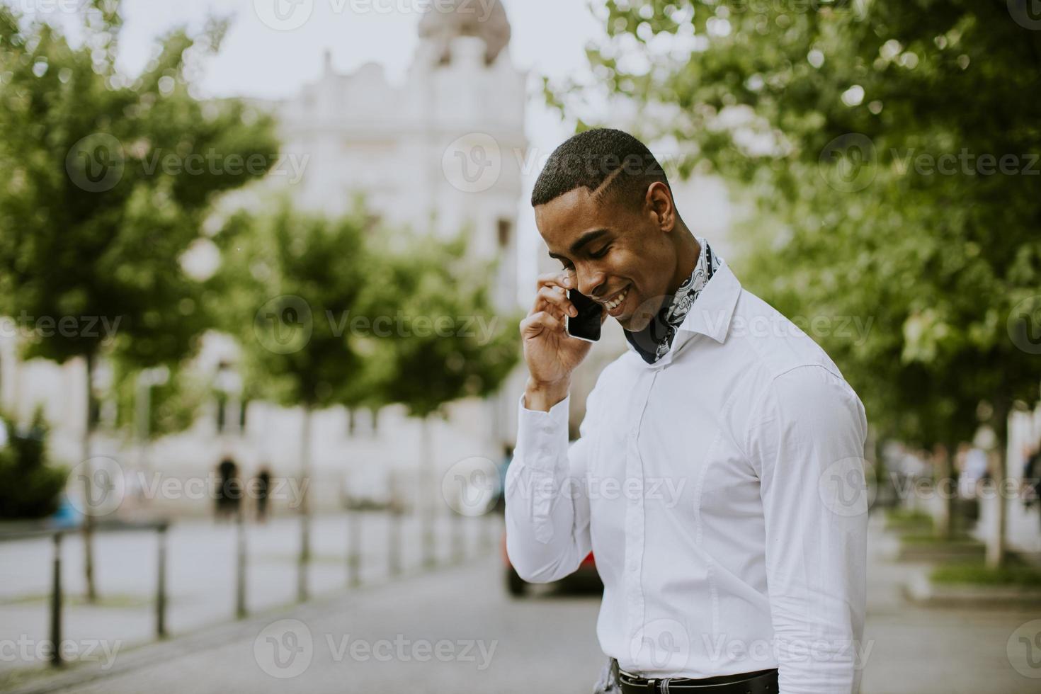 jonge Afro-Amerikaanse zakenman met behulp van een mobiele telefoon terwijl waitng voor een taxi in een straat foto