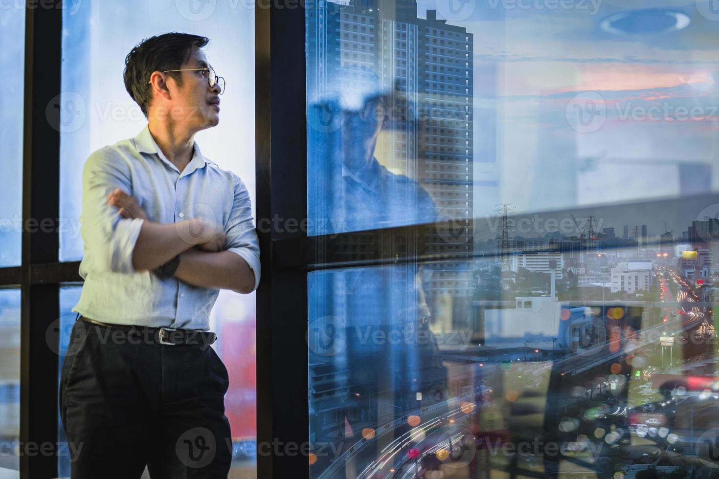 zakenman permanent bij raam van kantoorgebouw met uitzicht op stadsgezicht foto