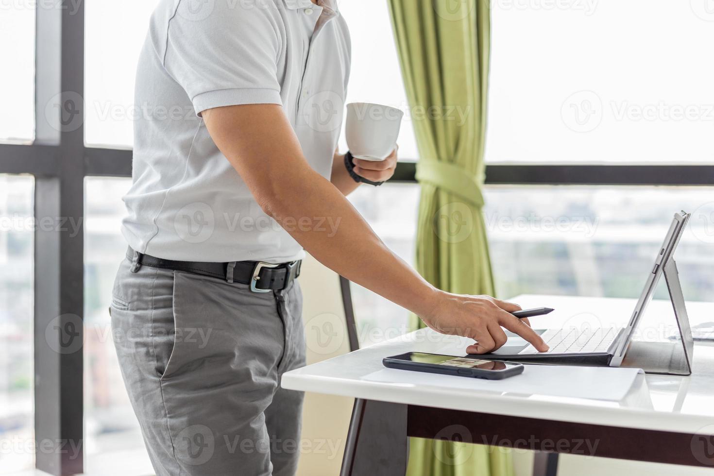 zakenman die e-mail op laptop controleert en kop koffie houdt foto