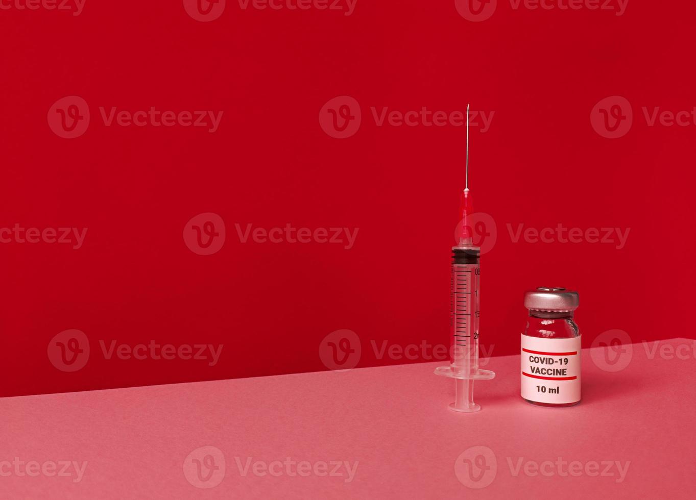 medische fles met covid 19-vaccin en spuit op rode achtergrond met gekantelde trendy skyline en kopieerruimte foto