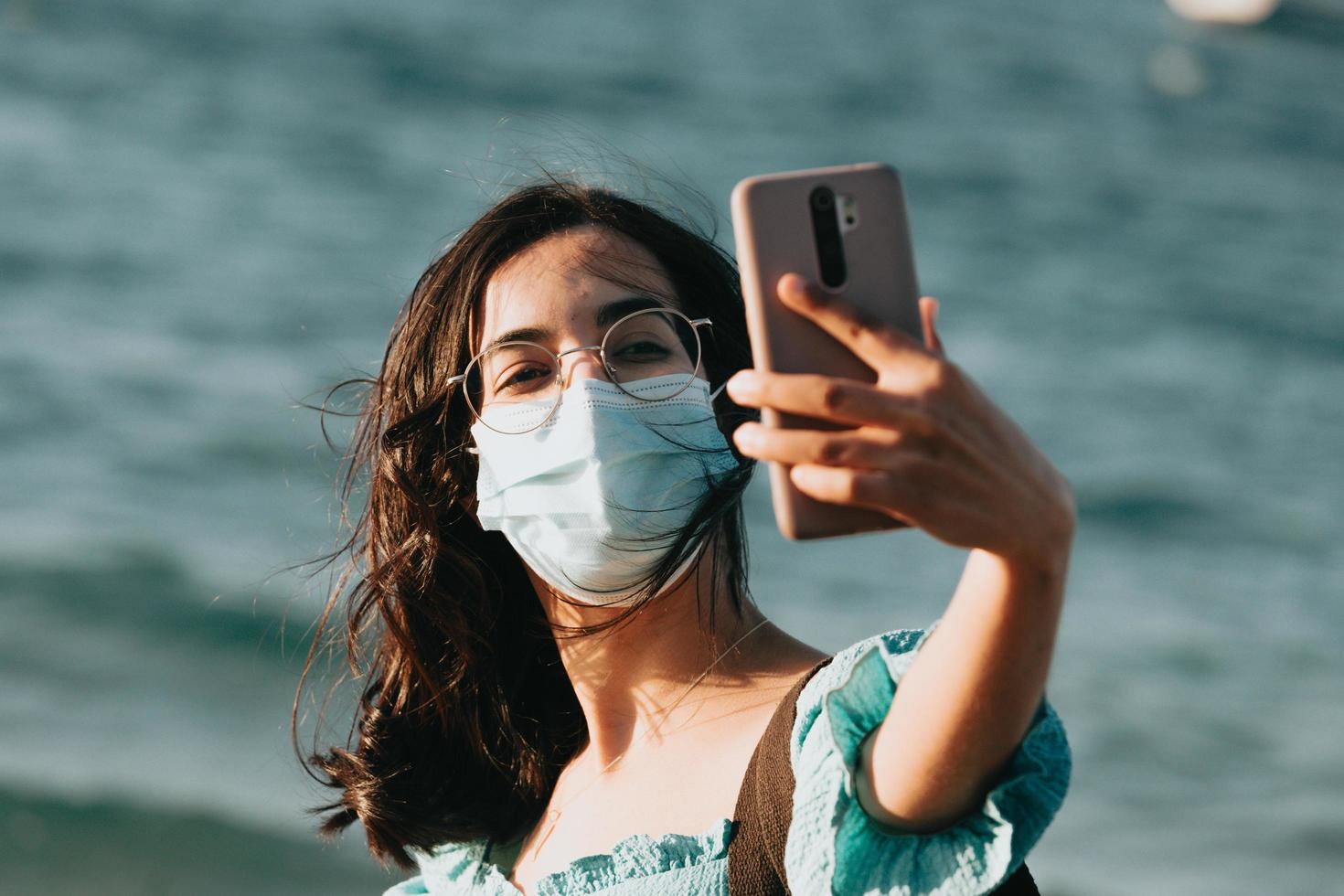 jonge vrouw op het strand met behulp van een masker tijdens het nemen van een selfie lifestyle concept zomerstijl foto