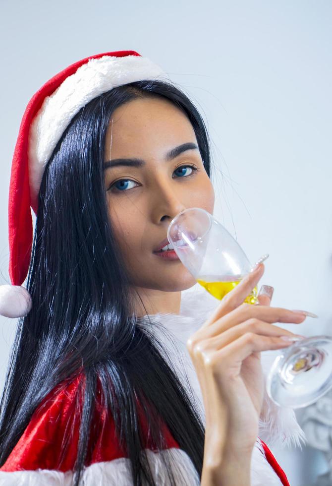 De aziatische vrouw die de hoed van de Kerstman draagt viert Kerstmis door gelukkig champagne te drinken foto