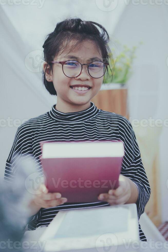 Aziatisch meisje Holding groot school- boek in hand- en toothy glimlachen met geluk foto