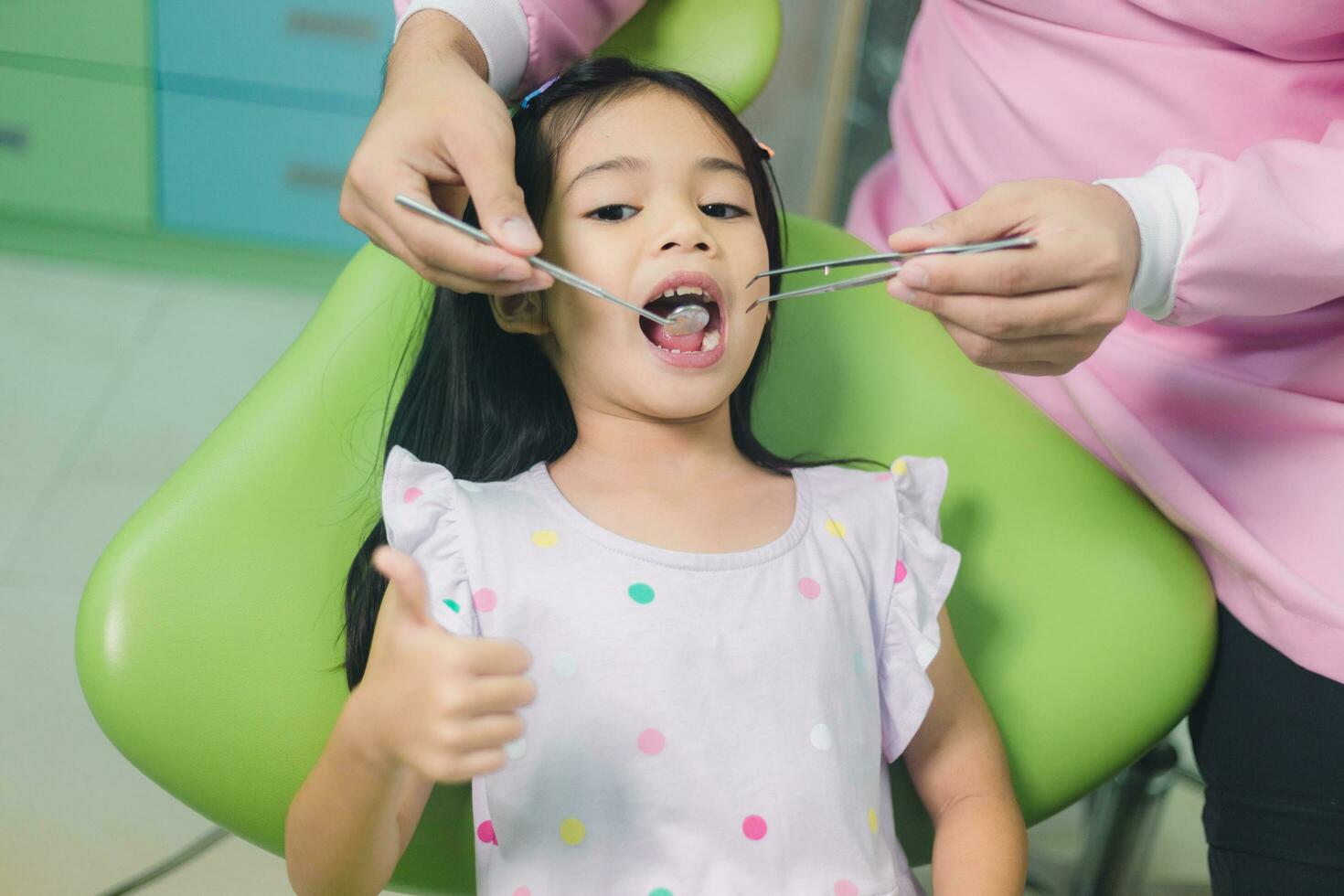 weinig Aziatisch meisje zittend Bij tandheelkundig stoel met Open mond gedurende mondeling controleren omhoog terwijl dokter. bezoekende tandarts kantoor. geneeskunde en stomatologie concept foto