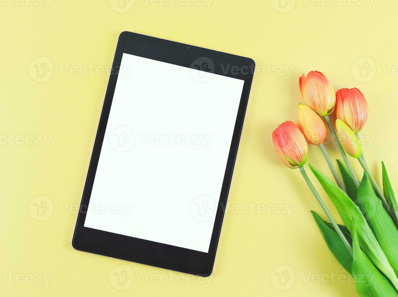 vlak leggen van digitaal tablet met blanco wit scherm, tuip bloemen geïsoleerd Aan geel achtergrond. foto