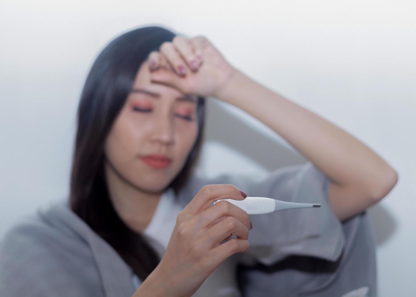 Aziatische vrouw is ziek door ziekte en houdt een thermometer vast foto