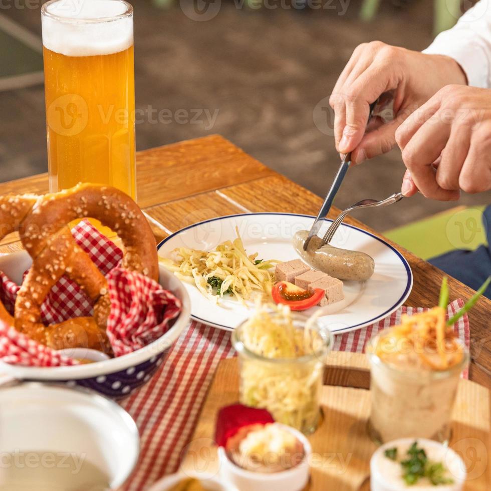 man snijden smakelijke Duitse worst met bier foto