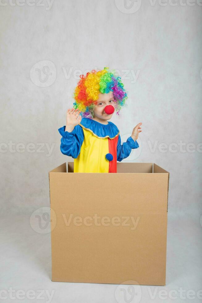 jongen van vijf jaren gekleed in de kostuum van een clown blijft in een karton papier doos. foto