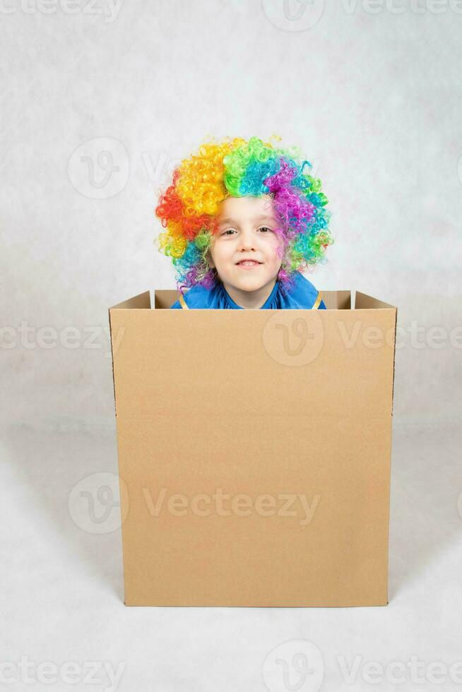 jongen van vijf jaren gekleed in de kostuum van een clown blijft in een karton papier doos. foto