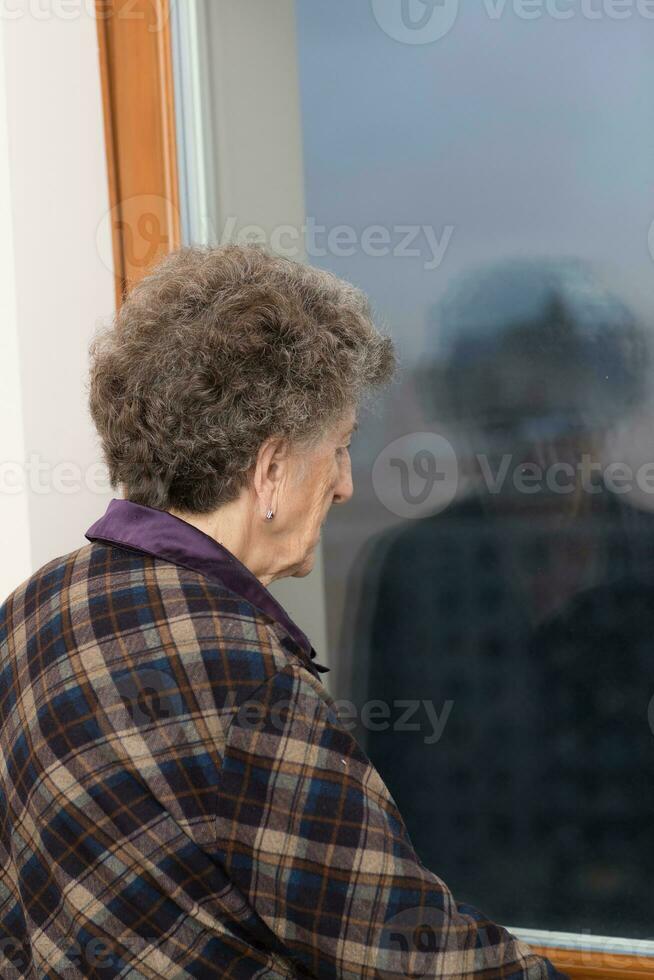 oud vrouw van 80 jaren oud blijft dichtbij naar de venster foto