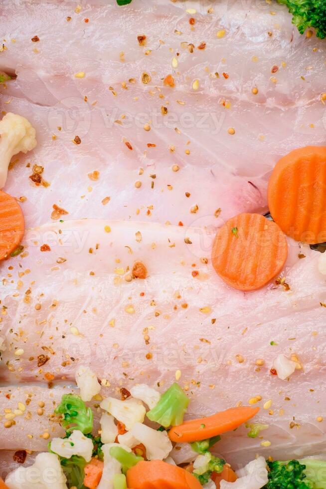 rauw zee bas vis filet met zout, specerijen en groenten in een bakken schotel foto