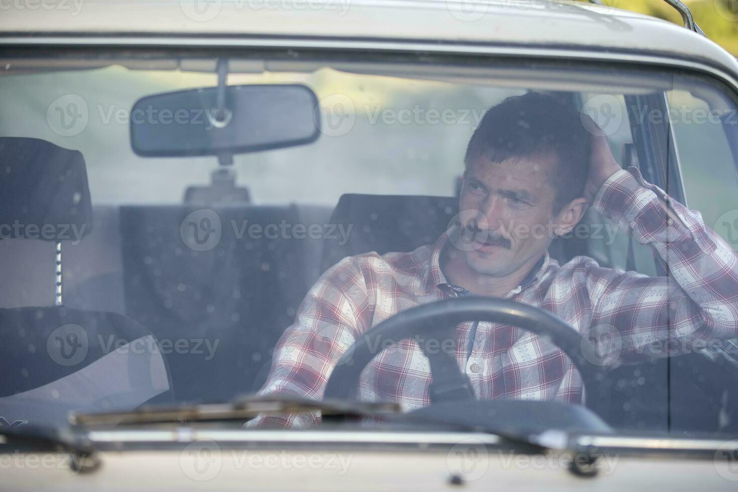 een Mens in een plaid overhemd zit in een oud auto. land jongen. foto