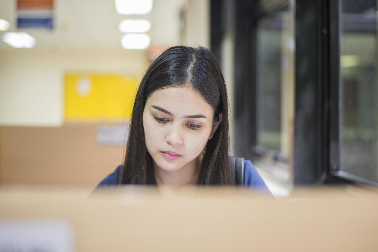 aantrekkelijke vrouwelijke Aziatische universiteitsstudent leesboek in bibliotheek foto