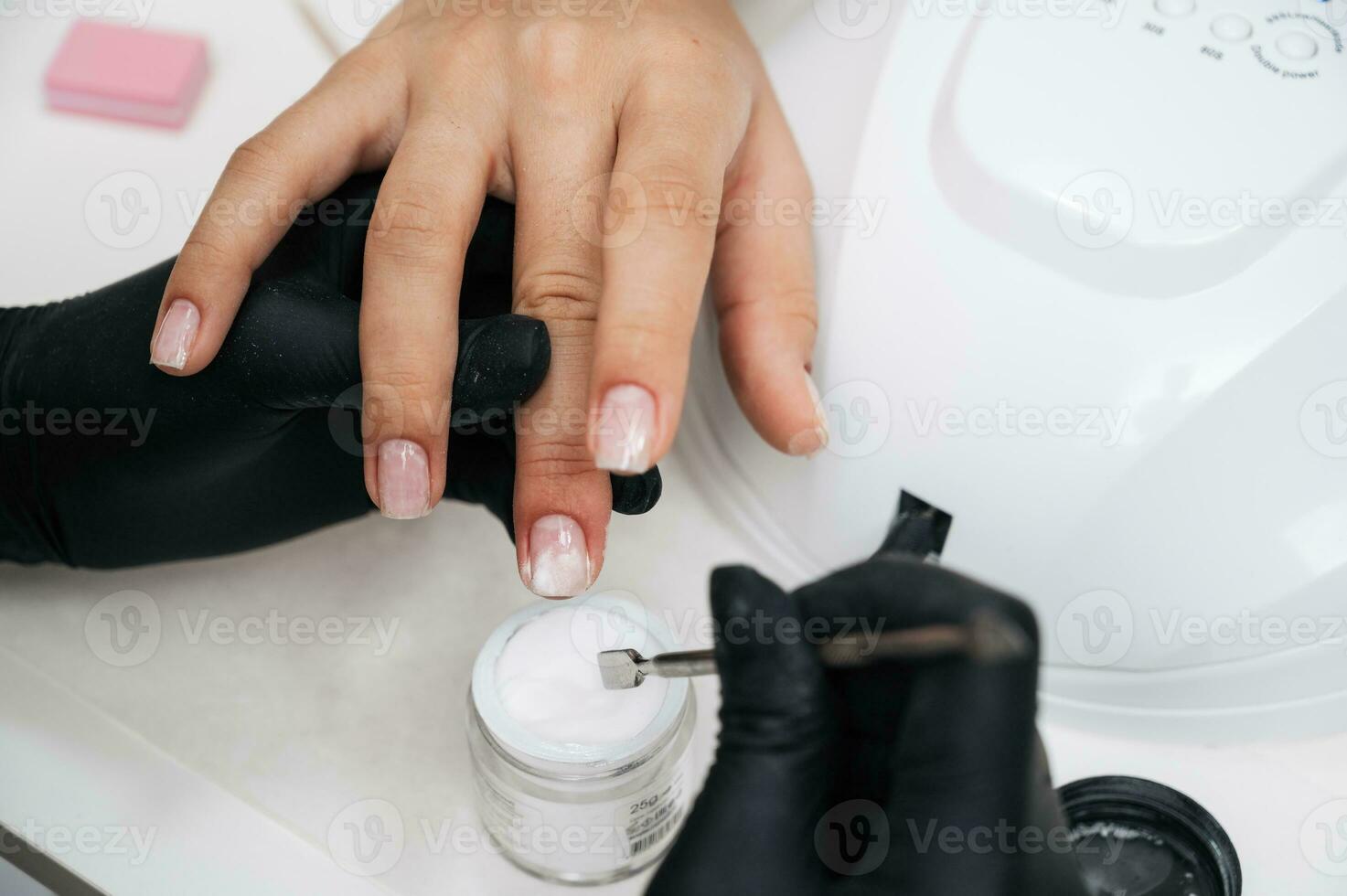 een manicure meester geeft een manicure naar een meisje in de salon. detailopname. de manicure meester versterkt de van de klant nagel met poeder. foto