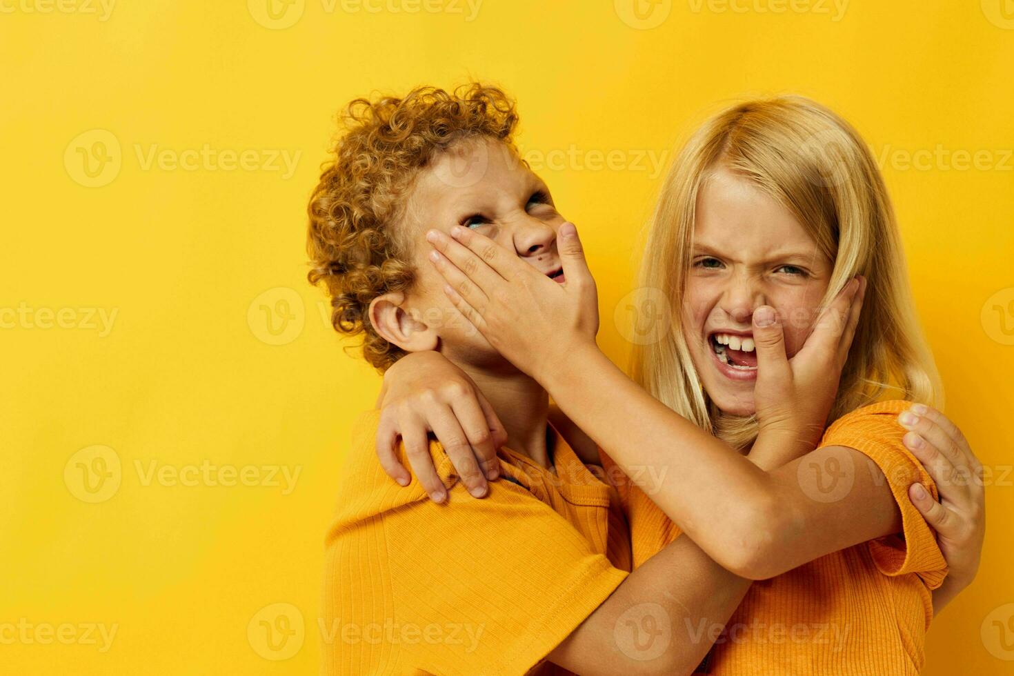 twee blij kinderen in geel t-shirts staand kant door kant kinderjaren emoties geel achtergrond foto