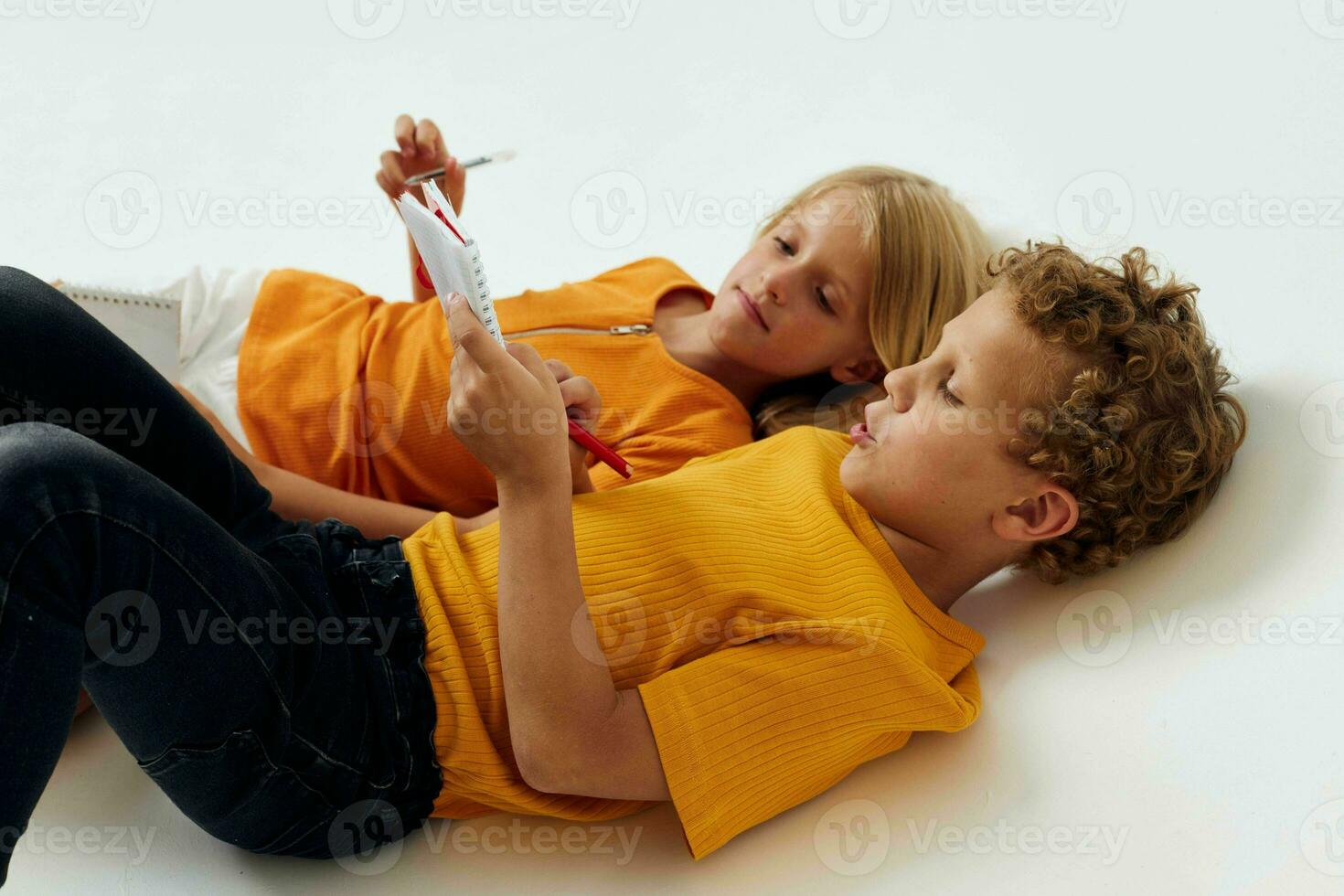 afbeelding van positief jongen en meisje liggen Aan de verdieping met blocnotes en potloden geïsoleerd achtergrond ongewijzigd foto