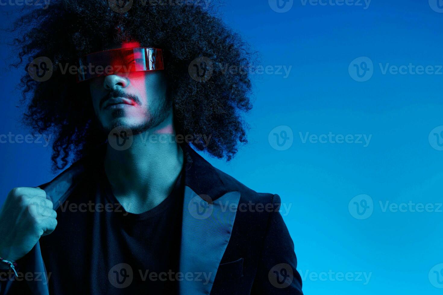 mode portret van een Mens met gekruld haar- Aan een blauw achtergrond vervelend rood zonnebril, multinationaal, gekleurde licht, trendy, modern concept. foto