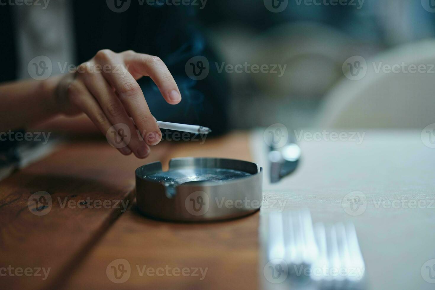 een vrouw met een sigaret in haar handen schudt de as in een asbakje, detailopname foto