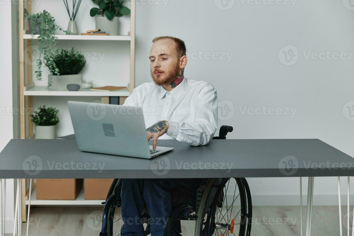 een Mens in een rolstoel een zakenman met tatoeages in de kantoor werken Bij een laptop, integratie in samenleving, de concept van werken een persoon met handicap, vrijheid van sociaal kaders foto