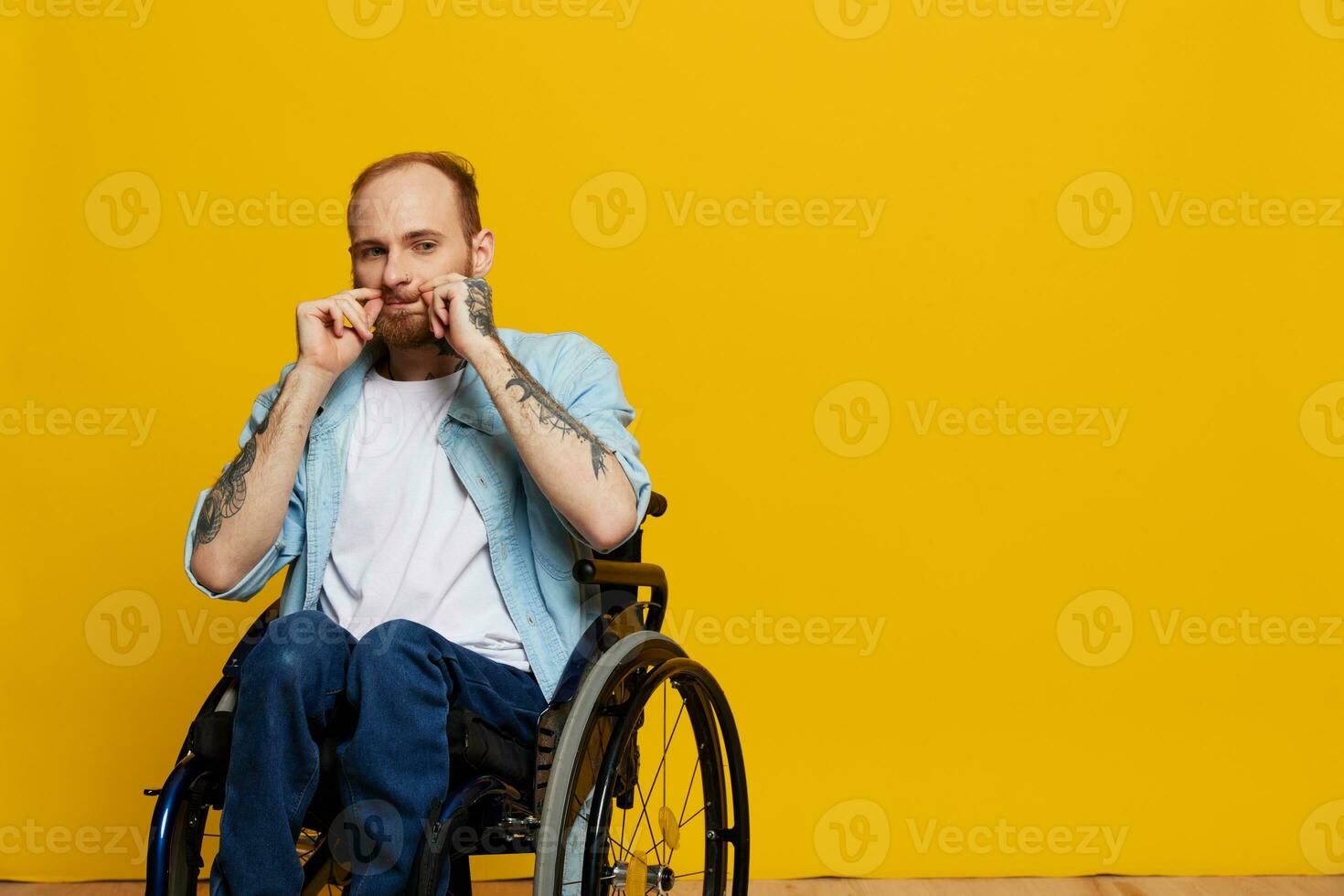 een Mens in een rolstoel looks Bij de camera, met tatoeages Aan zijn armen zit Aan een geel studio achtergrond, de concept van Gezondheid is een persoon met handicaps foto