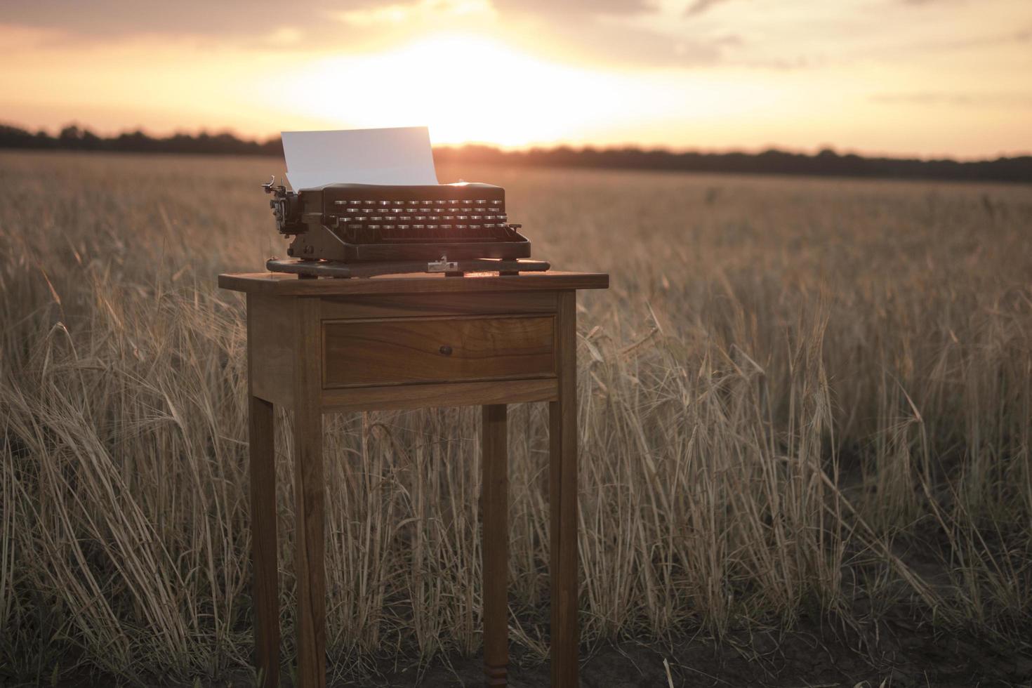 typemachine op een walnoot nachtkastje in een tarweveld bij zonsondergang foto