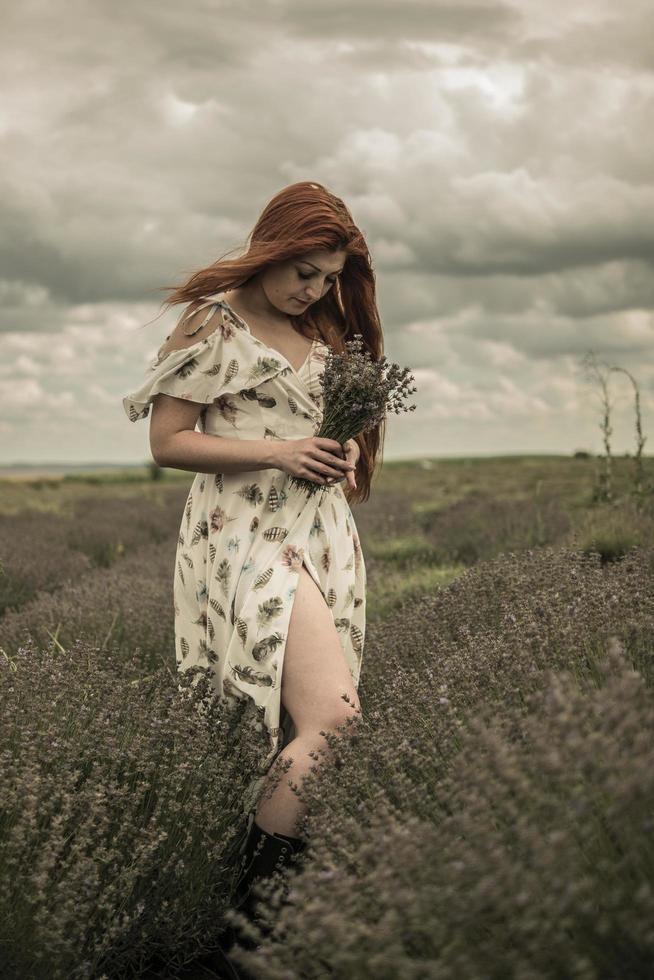 portret van een roodharig jong meisje in een witte jurk in een veld met een boeket lavendel foto