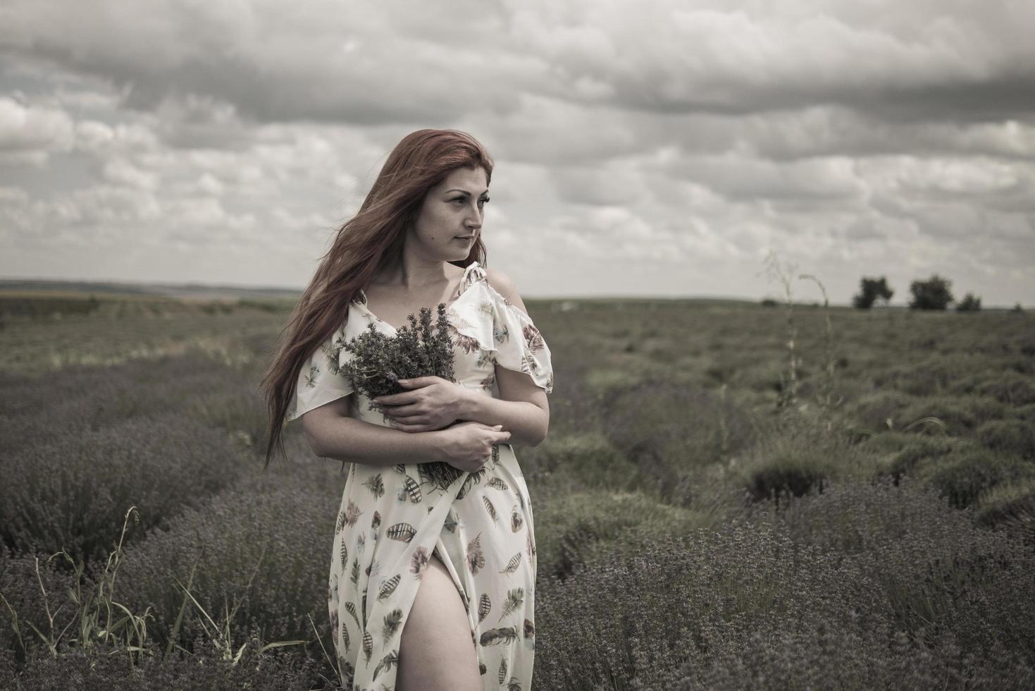 portret van een roodharig jong meisje in een witte jurk in een veld met een boeket lavendel foto