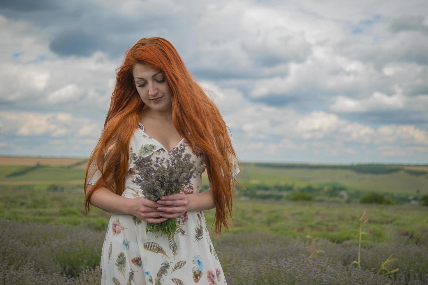 portret van een roodharig jong meisje in een witte jurk in een veld met een boeket lavendel foto