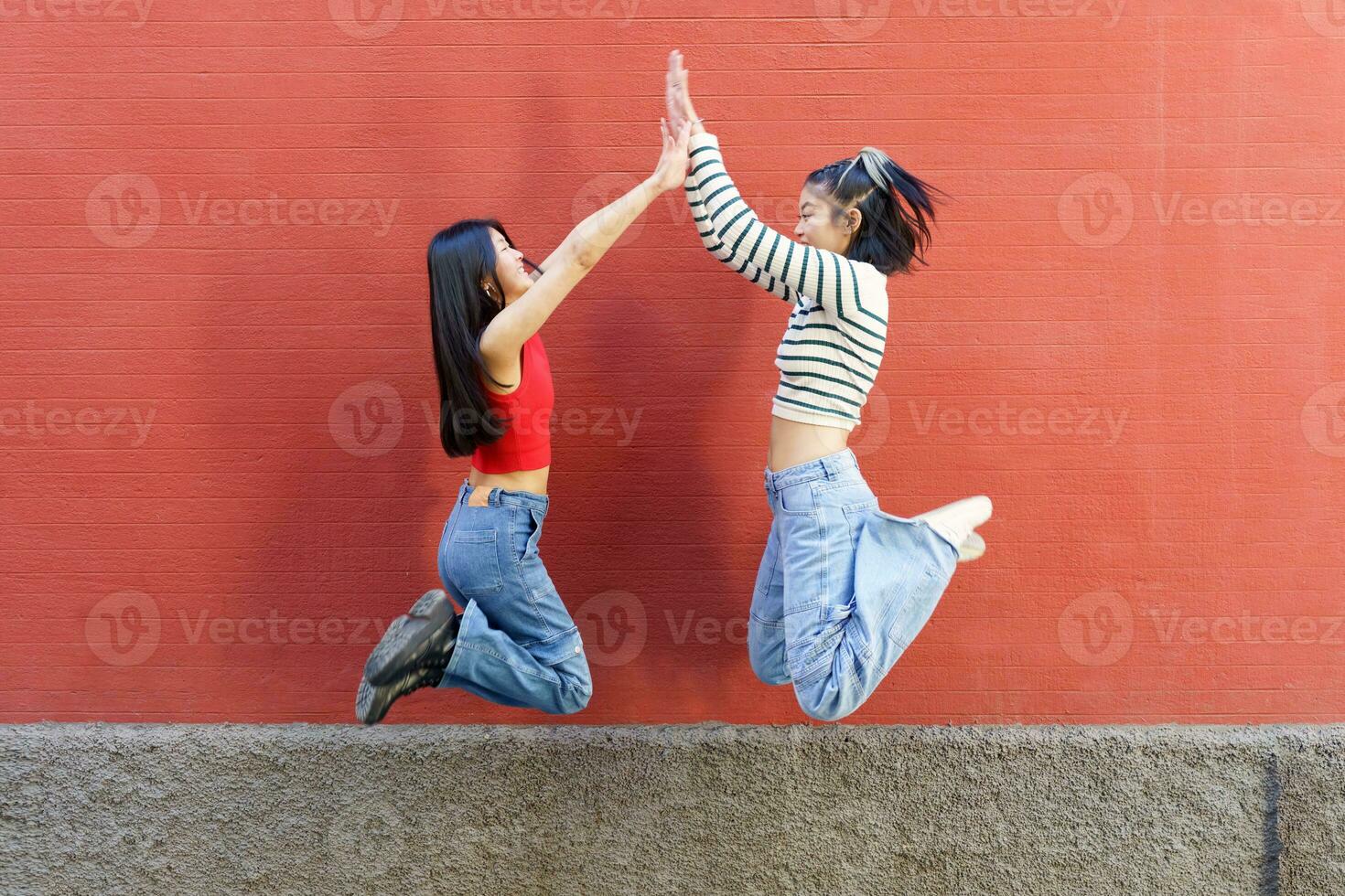 blij jong Aziatisch Dames geven hoog vijf terwijl jumping foto