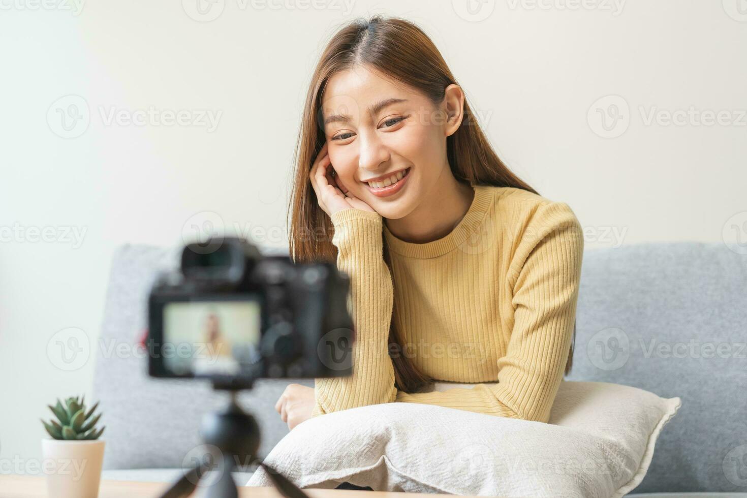 vlogger beïnvloeder, aantrekkelijk Aziatisch jong vrouw blogger, inhoud maker op zoek Bij camera, opname interview zitten Aan bank, praten Aan video het schieten sociaal media, leven uitzending met technologie Bij huis. foto