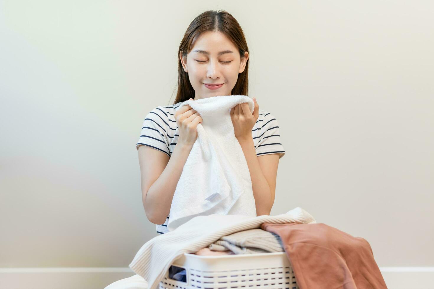 voelen zachtheid, glimlachen Aziatisch jong vrouw, meisje aanraken pluizig handdoek katoen, ruiken vers schoon kleren Aan tafel na wassen, de was, droog. huishouden werken Bij huis. wasserij en hulp in de huishouding. foto