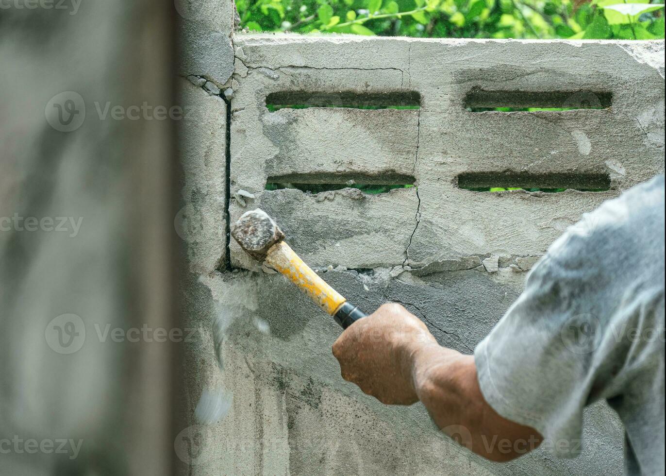 hand- van arbeider gebruik makend van hamer verpletterend en slopen Aan steen muur Bij bouw plaats foto