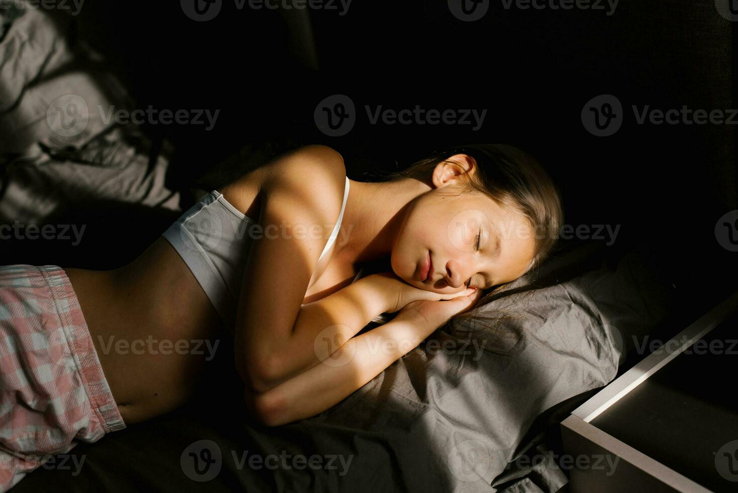 meisje slaapt Aan een bed met donker beddengoed in de zon en glimlacht in de vroeg ochtend- foto