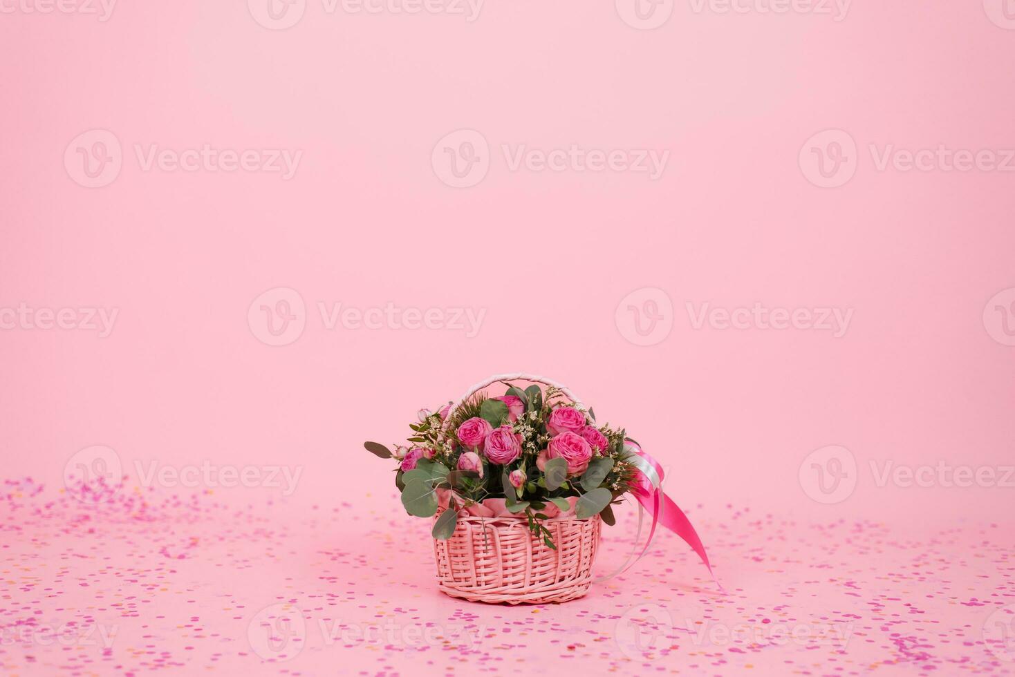 mooi boeket van roze rozen en eucalyptus takken in een geschenk mand Aan een roze achtergrond met confetti voor verjaardag, Valentijnsdag dag of mama's dag foto