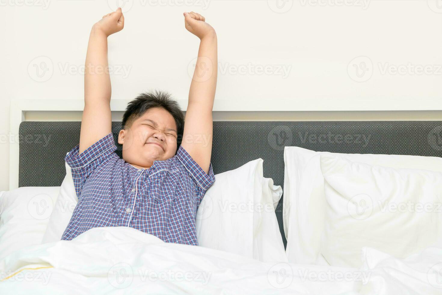 zwaarlijvig dik jongen wordt wakker omhoog en uitrekken Aan bed in ochtend, foto