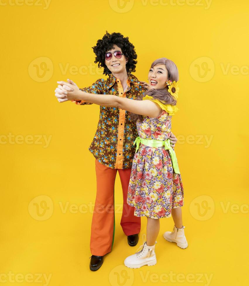 Aziatisch hippie paar jurk in 80s wijnoogst mode met kleurrijk retro kleding terwijl dansen samen geïsoleerd Aan geel achtergrond voor luxe kleding partij en knal cultuur concept foto