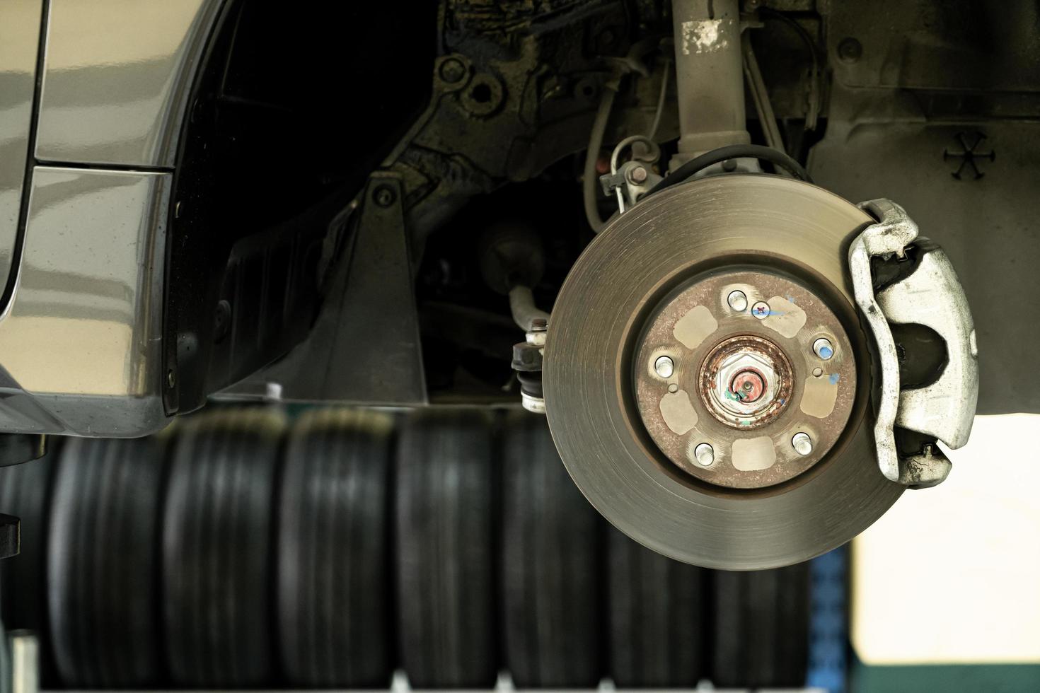 schijfauto close-up - monteur die auto-onderdelen losschroeft terwijl hij werkt onder een opgeheven auto - autoserviceconcept foto